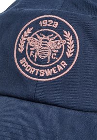 Dunkelblaues Baseballcap aus strukturiertem Stoff mit einem gestickten, rosafarbenen, runden Logo einer Biene, Lorbeerblättern und dem Text "1923 SPORTSWEAR."