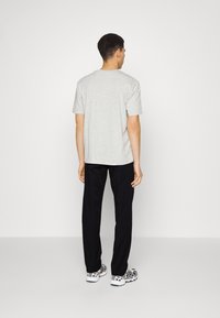 Light gray short-sleeve t-shirt with a round neckline, paired with black trousers and patterned sneakers, viewed from the back.