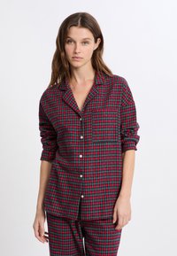 Conjunto de pijama de cuadros rojos y verdes con una camisa abotonada que incluye un bolsillo y mangas enrolladas, hecho de una tela suave con un corte relajado.