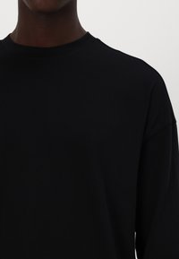 Schwarzes Langarm-T-Shirt mit Rundhalsausschnitt. Der Stoff wirkt weich und glatt, mit einer lockeren Passform ohne sichtbare Muster oder Akzente.