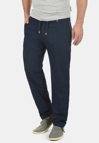 Pantaloni cu talie elastică de culoare bleumarin, cu închidere cu șnur, confecționați dintr-un material ușor, având buzunare laterale și o croială lejeră.