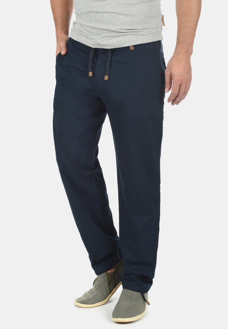 Pantaloni cu talie elastică de culoare bleumarin, cu închidere cu șnur, confecționați dintr-un material ușor, având buzunare laterale și o croială lejeră.