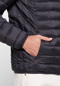 Czarna pikowana kurtka puchowa z przeszywanym wzorem, wyposażona w kieszeń na zamek po lewej stronie oraz elastyczne mankiety dla pewnego dopasowania.