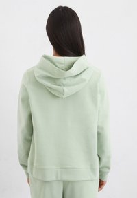 Lichtgroene hoodie met een relaxte pasvorm, zachte textuur, geribbelde manchetten en een kangoeroezak, van achteren weergegeven.