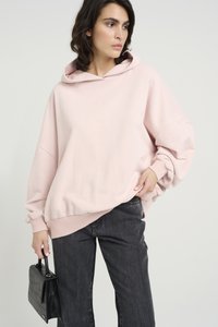 Svetlo roza prevelik hoodie z sprednjim žepom in rebrastimi robovi. V kombinaciji z temno sivimi hlačami ravnega kroja in črno teksturirano torbico.