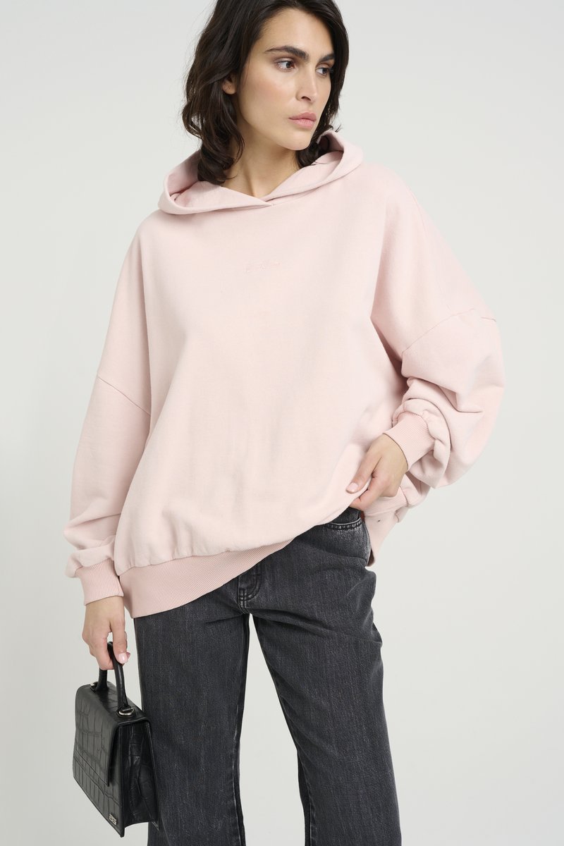 Svetlo roza prevelik hoodie z sprednjim žepom in rebrastimi robovi. V kombinaciji z temno sivimi hlačami ravnega kroja in črno teksturirano torbico.