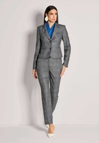 Grijs geruite pak met een getailleerd jasje en rechte broekspijpen. Vergezeld van een blauwe sjaal en witte puntige schoenen. Grote ronde oorbellen.