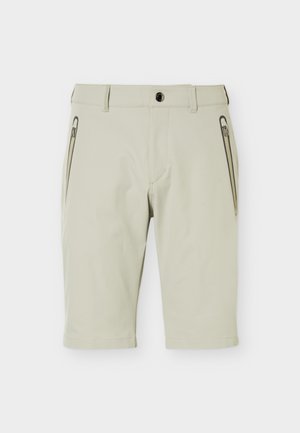 Φωτεινά μπεζ σορτς έως το γόνατο με μπροστινό κουμπί, θηλιές για ζώνη και πλευρικές τσέπες με φερμουάρ σε λευκό απλό φόντο.