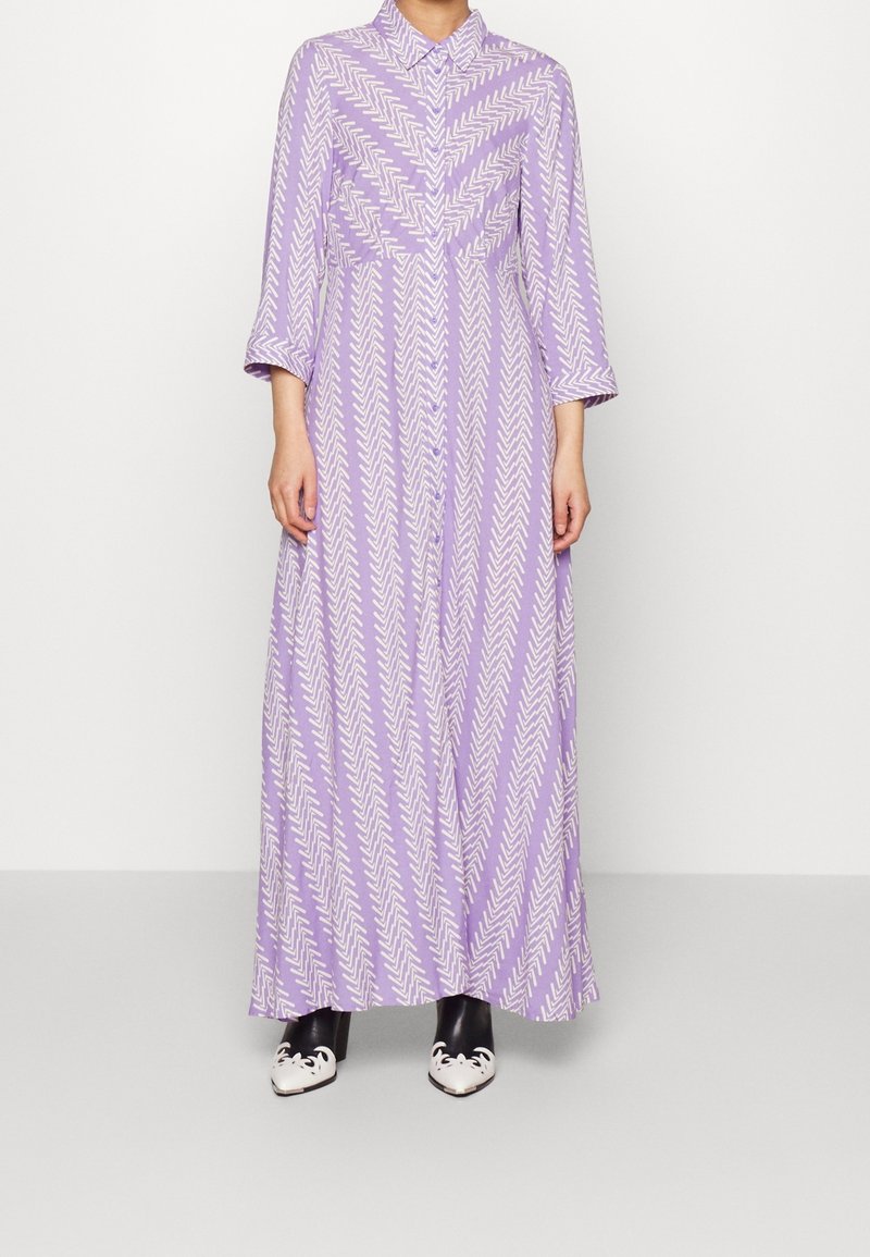 Lång lavendelfärgad klänning med ett chevronmönster, försedd med krage och trekvartsärmar. Matchas med svarta och vita klackskor.