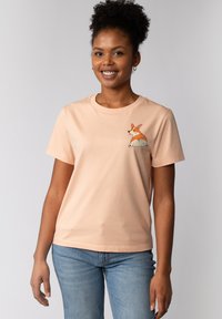 Perzikkleurig katoenen t-shirt met een speelse corgi-afbeelding op de linkerborst. Korte mouwen, ronde hals en een relaxte pasvorm.