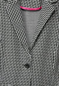 Blazer à motifs noirs et blancs avec un revers cranté, une fermeture à un bouton noir et un accent rose le long du col intérieur.