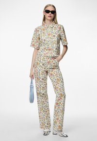 Camisa corta con estampado floral y pantalones a juego en tonos claros. Tacones plateados y un bolso azul completan el conjunto. Textura de tela suave.