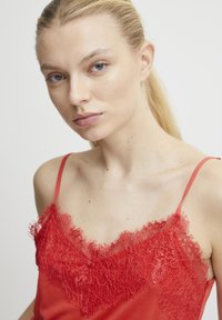 Camisola de encaje roja con tirantes finos y un borde de encaje floral en el escote, con una suave tela de satén debajo.