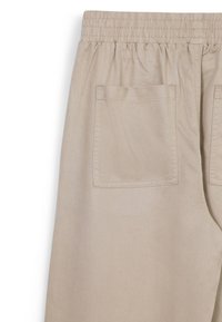 Helle beigefarbene Baumwollhosen mit einem elastischen Bund, einer einzelnen Gesäßtasche und einer glatten Textur mit einem subtilen Glanz.