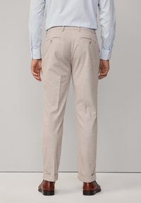 Beige trousers with a straight fit, featuring two back pockets with button closures. Rolled cuffs and fabric texture visible.
