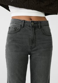 Jeans de mezclilla gris con cintura alta, diseño de cinco bolsillos, cierre frontal con botón y detalles de desgaste sutiles a lo largo de los muslos.