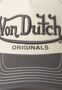 Cap with cream fabric and a dark gray brim. Features embroidered "Von Dutch" logo and "ORIGINALS" text, both in dark thread. Accented with white stitching.