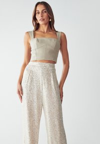 Top corto di un leggero beige con scollatura quadrata e spalline larghe, abbinato a pantaloni larghi scintillanti e con paillettes in una tonalità di crema.