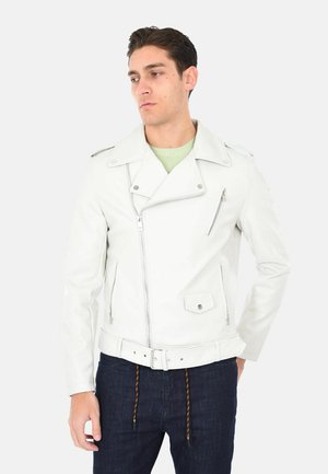 Giacca da motociclista in pelle bianca con colletto a punte, zip frontale asimmetrica e vita con cinturino. Abbinata a jeans scuri.