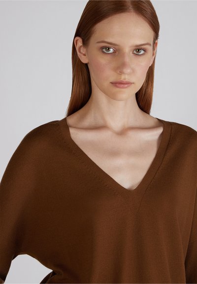 Bruine V-hals trui met een losse, oversized pasvorm, gemaakt van zacht materiaal. Eenvoudig ontwerp, textuurafwerking en minimale stikseldetails.
