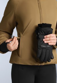 Brown, textured jacket with a zippered pocket; black gloves with a smooth finish held in the other hand; fitted with black pants.