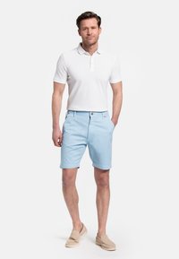 Witte polo, lichtblauwe shorts en beige instappers. Gepolijste, casual uitstraling. Shorts hebben een knoopsluiting en zakken.