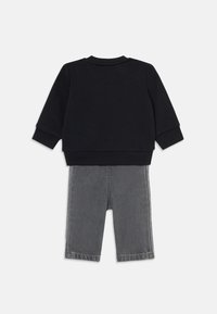 Sweatshirt noir avec des poignets côtelés associé à un pantalon en denim gris à coupe droite et des coutures contrastées.
