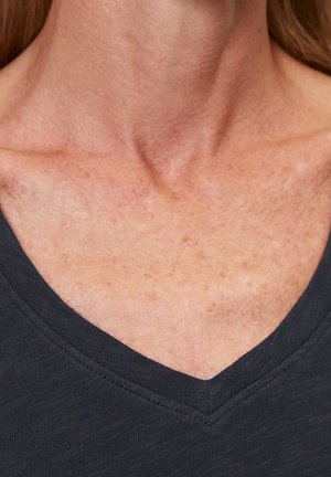 Maglietta nera con scollo a V in tessuto strutturato, che mette in risalto una linea del collo liscia e dettagli di cucitura. La vestibilità è comoda, adatta per un look casual.