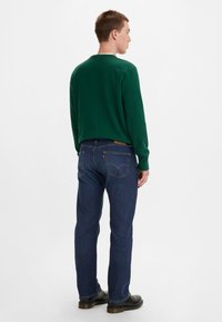 Grüner Rundhalsausschnitt-Pullover, blaue Jeans und schwarze Stiefel. Weiche Textur, reguläre Passform. Die Jeans haben Gesäßtaschen und ein Markenlabel.