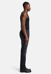 Zwarte tanktop gecombineerd met donkergrijze jeans, met een slim fit en subtiele textuur. Het onderwerp draagt zwarte schoenen met een gepolijste afwerking.