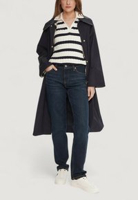 Marineblå regnjakke, hvid og marineblå stribet striktrøje, mørke jeans og hvide sneakers. Jakken har krave og trykknapper.