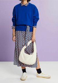 Sudadera azul con cuello redondo sobre un vestido a cuadros en azul y rosa. Un bolso blanco y zapatillas de color crema completan el conjunto.