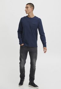 Tengerészkék, hosszú ujjú ing, amelyen mellzseb található, sötét, slim fit farmernadrággal és fekete sportcipővel párosítva. Az anyag lágy tapintású, texturált felületű.