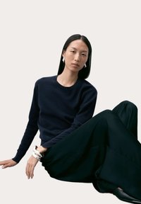 Marinblå ulltröja med rund hals, kombinerad med vida svarta byxor. Märkbart silverarmband och geometriska örhängen ger accenter. Släta texturer.