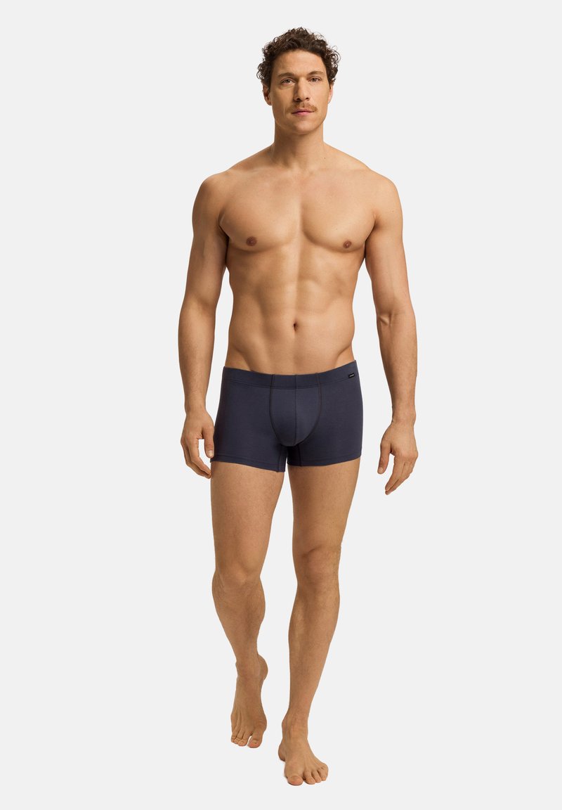 Tmavě modré pánské boxerky s přiléhavým střihem, moderním pasem a minimem švů. Model je zobrazen s odhaleným trupem a bez obuvi.