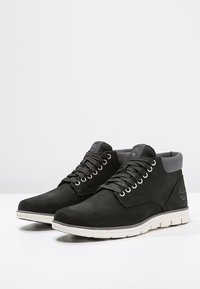 Svarta mockakängor med grå accenter, runda skosnören och en vit gummisul. Har logotypdetalj på sidan.