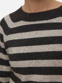 Zbliżenie osoby w beżowym i ciemnobrązowym swetrze z poziomymi paskami, z okrągłym dekoltem.