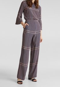 Mönstrad jumpsuit i marinblått, rött och beige. Har vida ben, långa ärmar med utsvängda manschetter och sidofickor. Geometriskt mönster över hela.