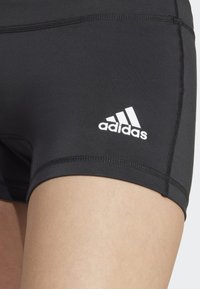 Pantaloni sportivi neri con vestibilità aderente, texture liscia e logo Adidas ricamato in bianco sulla coscia. Cuciture rinforzate visibili.