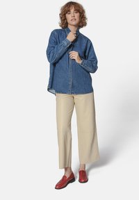 Jeans srajca z gumbom in dolgimi rokavi, v kombinaciji z sijajnimi bež širokimi hlačami in rdečimi usnjenimi čevlji brez pet, ki imajo teksturo.