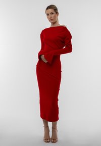 Abito midi rosso a coste con scollatura off-shoulder, lunghe maniche svasate, orlo asimmetrico e tessuto testurizzato. Completato con eleganti tacchi neutri.