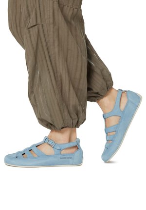 Hellblaue Wildlederschuhe mit Ausschnitten und Knöchelverschluss, kombiniert mit lockeren, olivgrünen Haremshosen mit vertikalen Streifen.