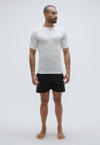 T-shirt de sport blanc à manches courtes avec une texture lisse, associé à un short noir. Présente une coupe ajustée et un logo sur la poitrine.
