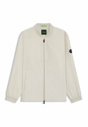 Lichtbeige bomberjack met een hexagonaal patroon, voorritssluiting, twee zijzakken en een zwart accent op de linkermouw.