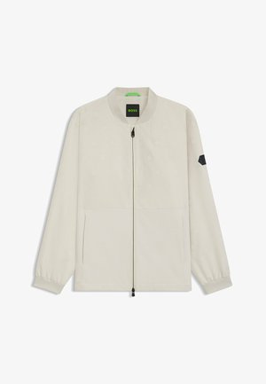 Jasno beżowa kurtka bomberka z heksagonalnym wzorem, zamek błyskawiczny z przodu, dwie boczne kieszenie oraz czarny akcent na lewym rękawie.