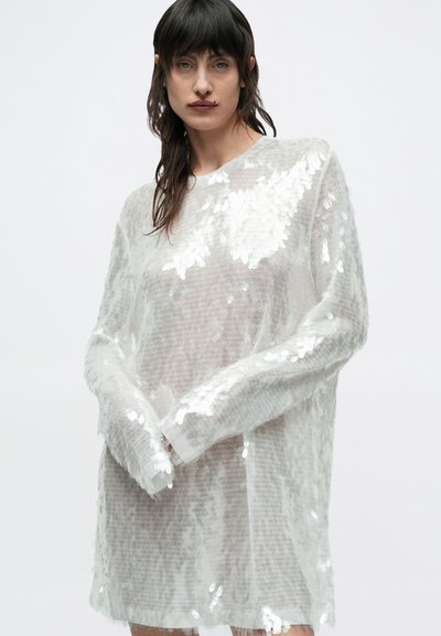 Διαφανές λευκό φόρεμα πουλόβερ με μακριά μανίκια, υφή στην επιφάνεια, καλυμμένο με αντανακλαστικές παγιέτες και χαλαρή εφαρμογή.