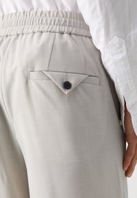 Pantaloni grigi chiari in tessuto testurizzato, con vita elastica e una tasca posteriore con patta triangolare e dettaglio a bottone.