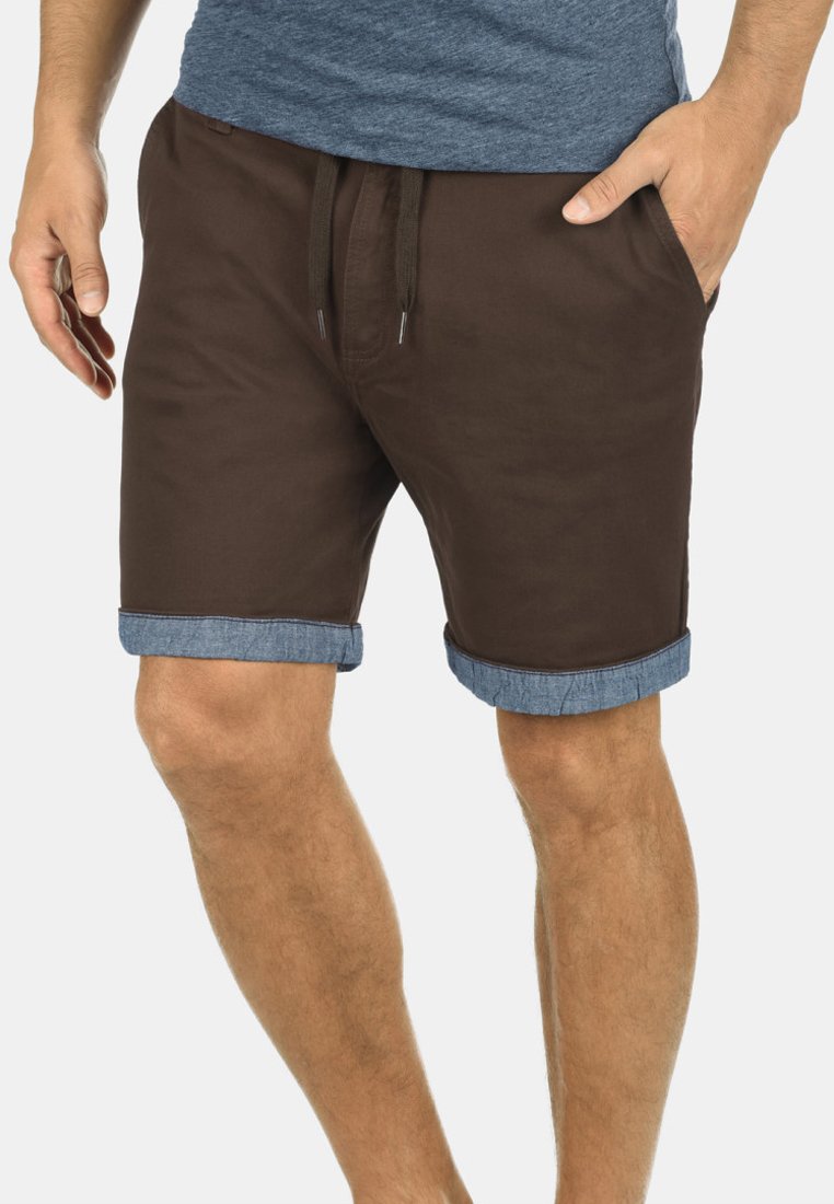 Shorts marron avec des poignets en denim retournés, dotés d'une taille à cordon et d'une texture lisse. Le matériau semble léger et décontracté.