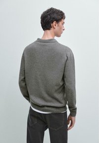 Pullover grigio a maglia con colletto, polsini e orlo a coste, caratterizzato da una finitura testurizzata. Indossato sopra una camicia bianca, mostrato di schiena.