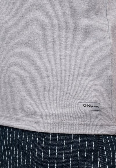 Γκρι ριμπ υφασμάτινο πουκάμισο με μικρή ετικέτα "Les Benjamins" πάνω από τη μέση μπλε παντελονιού με ρίγες.